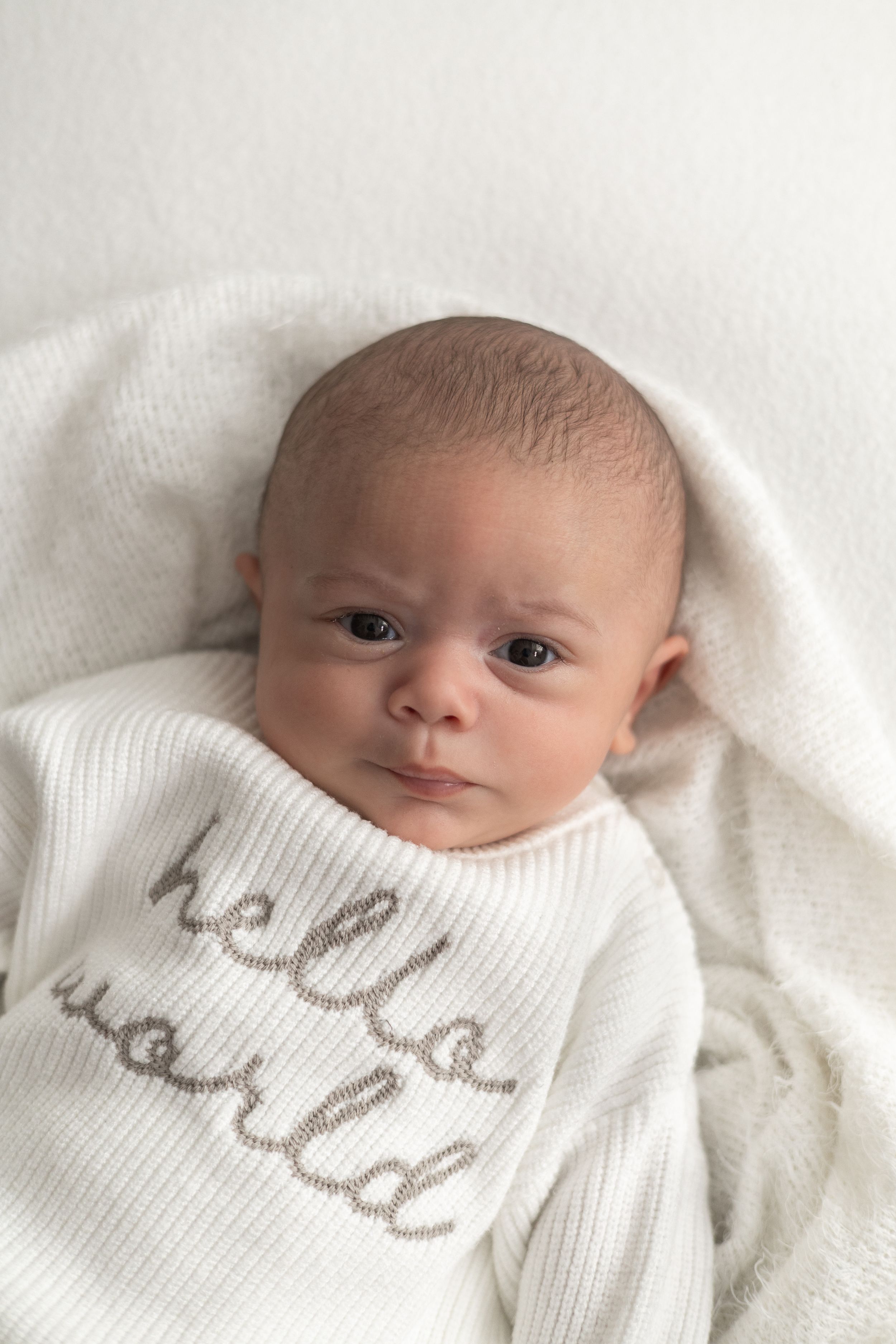 Newborn baby wrapped in a white knit blanket wearing a white onesie older newborn photographer Nottingham cosy home studio