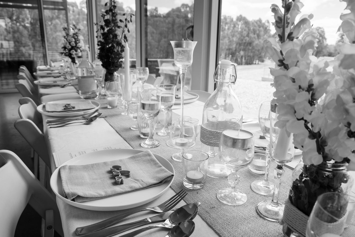 Black and white photo of an elegantly set dining table with crystal glasses, white flowers, and fine tableware for a formal event.