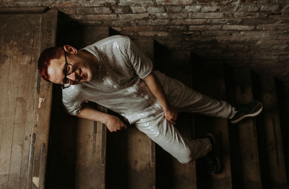 Man in white shirt and glasses smiling on rustic wooden stairs in an old brick building.