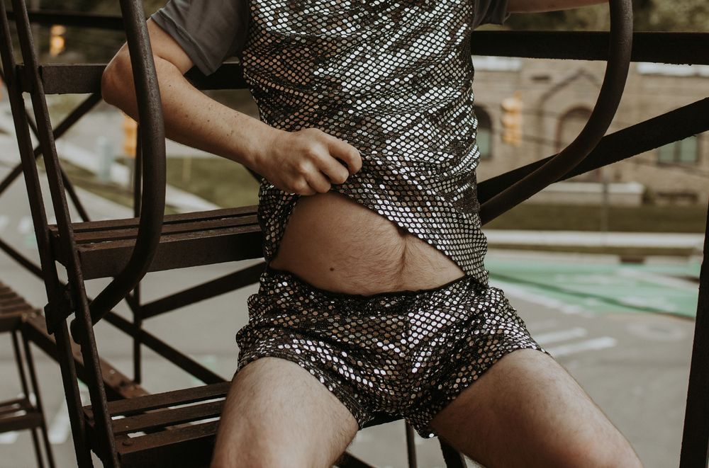 Person wearing shiny silver sequin matching set outfit lifting shirt on metal staircase.