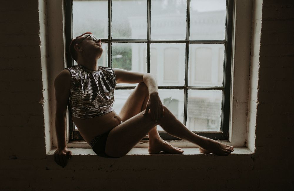 Woman in lingerie sitting on windowsill in moody dark room with natural light.