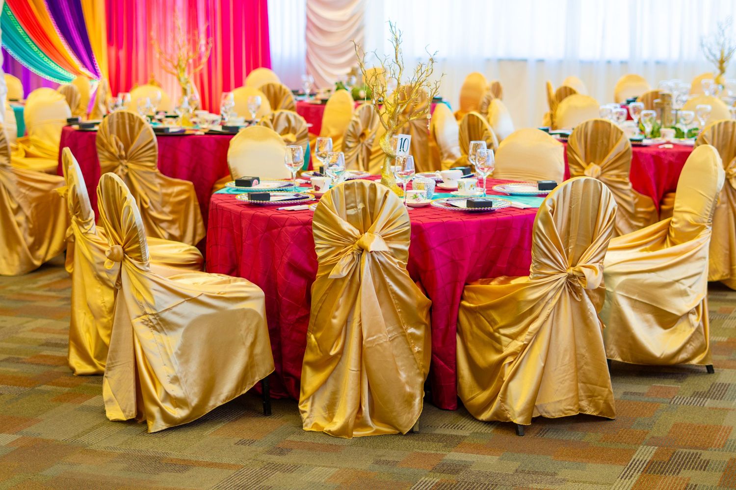 Elegant banquet hall with gold satin chair covers and pink tablecloths set for a formal event or wedding reception.