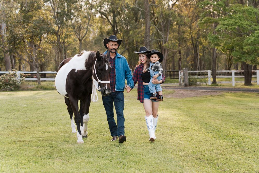 Family in cowboy hats walks with a paint horse on a green ranch pasture during a family photoshoot in sydney with a horse