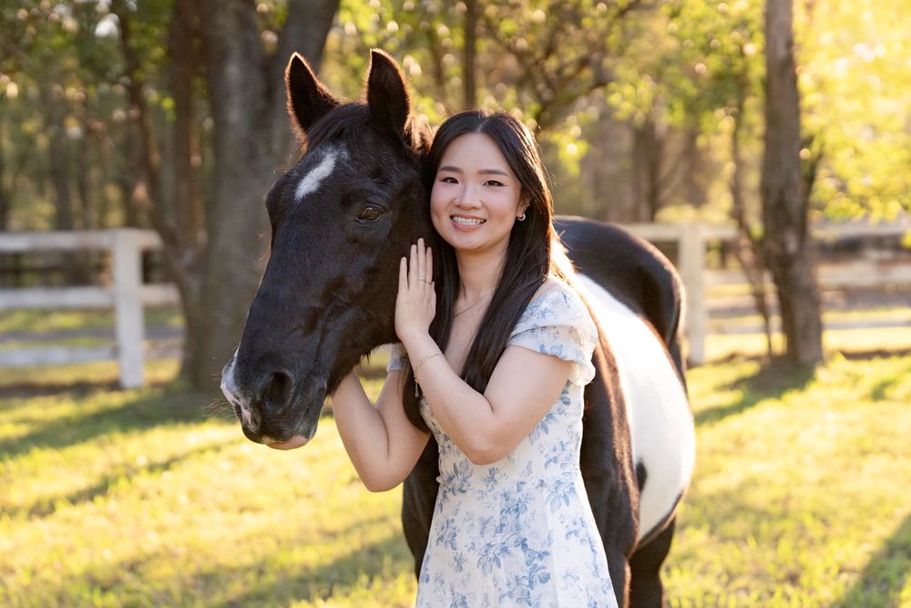 Young woman in floral dress smiling beside a black and white horse on a sunny green farm during a portrait photoshoot with a horse in Sydney