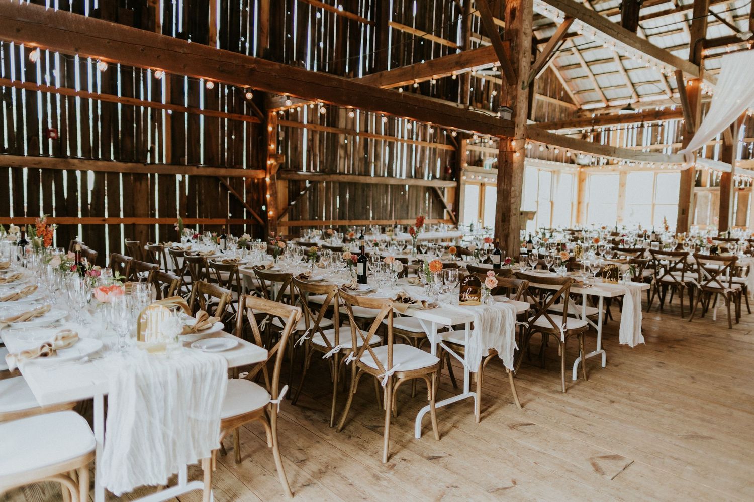 Barn wedding reception layout showing harvest tables arranged in long parallel rows with open guest circulation pathways.