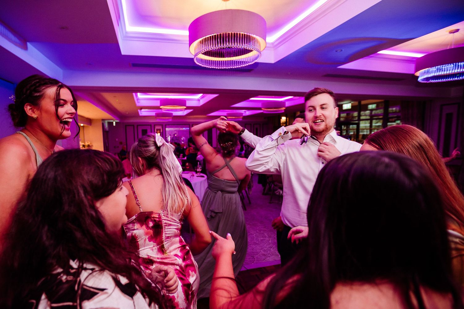 People dancing and celebrating at a lively party event with purple lighting.