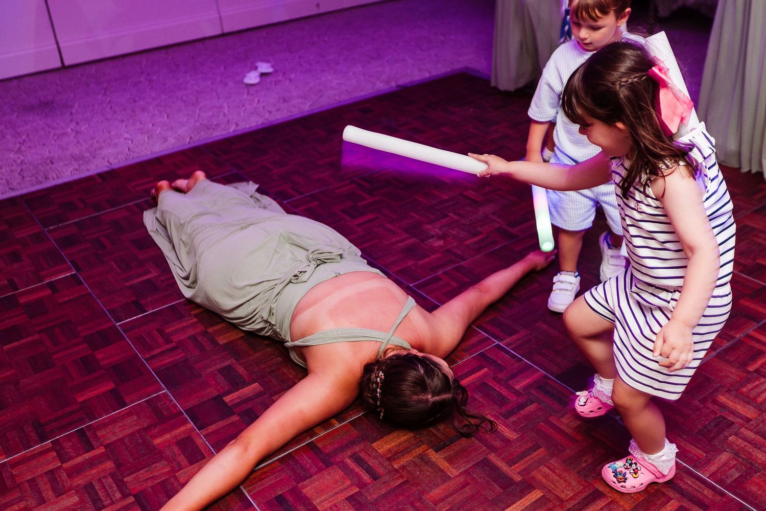 Children playing with foam noodles on a dance floor at a party event.