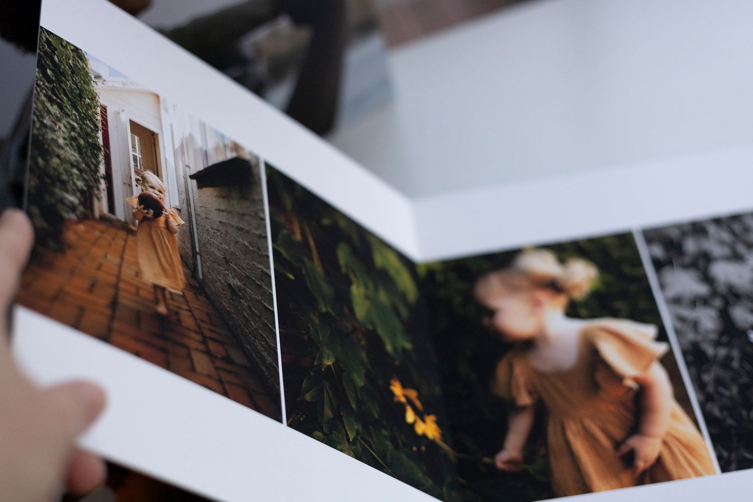 Open photo album displaying two portraits of a young girl in an orange dress among lush greenery and rustic settings.