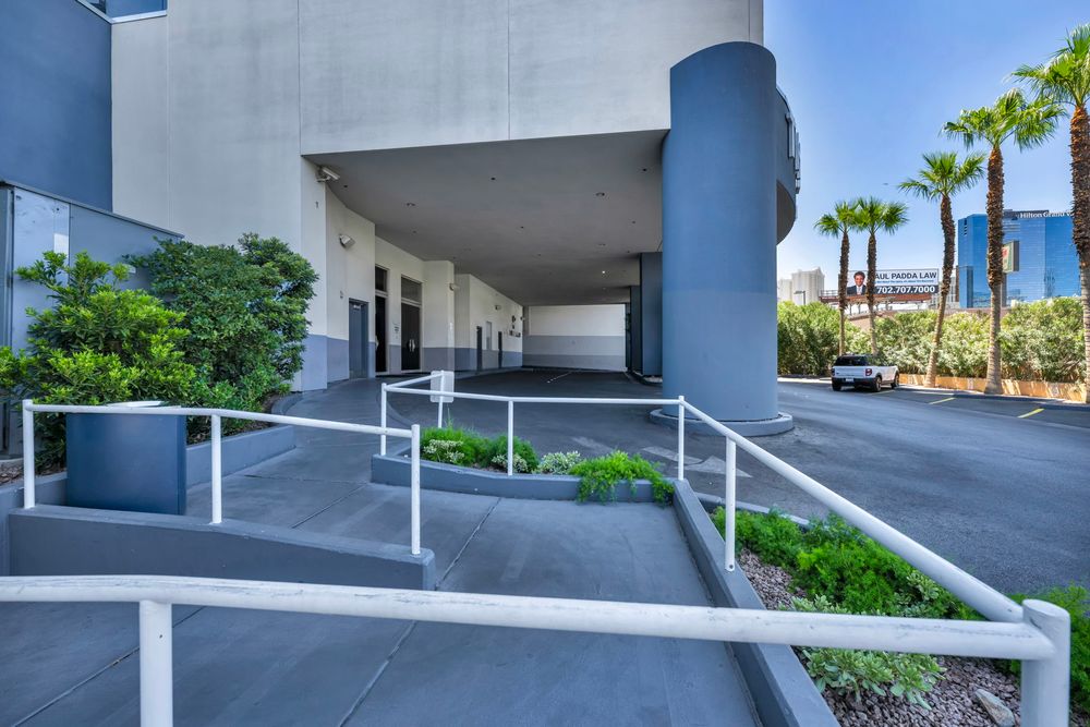 Modern hotel entrance with accessible ramp, covered driveway, and palm tree landscaping.