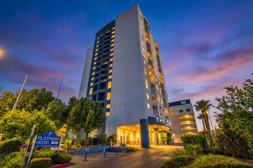 The Platinum Hotel tower glows at dusk surrounded by lush trees near the Las Vegas Strip.