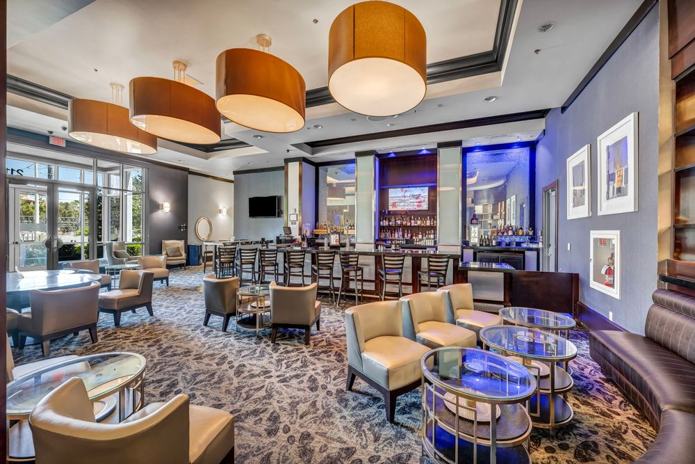 Upscale hotel lounge bar with stylish pendant lights, plush seating, and blue-lit bar area.