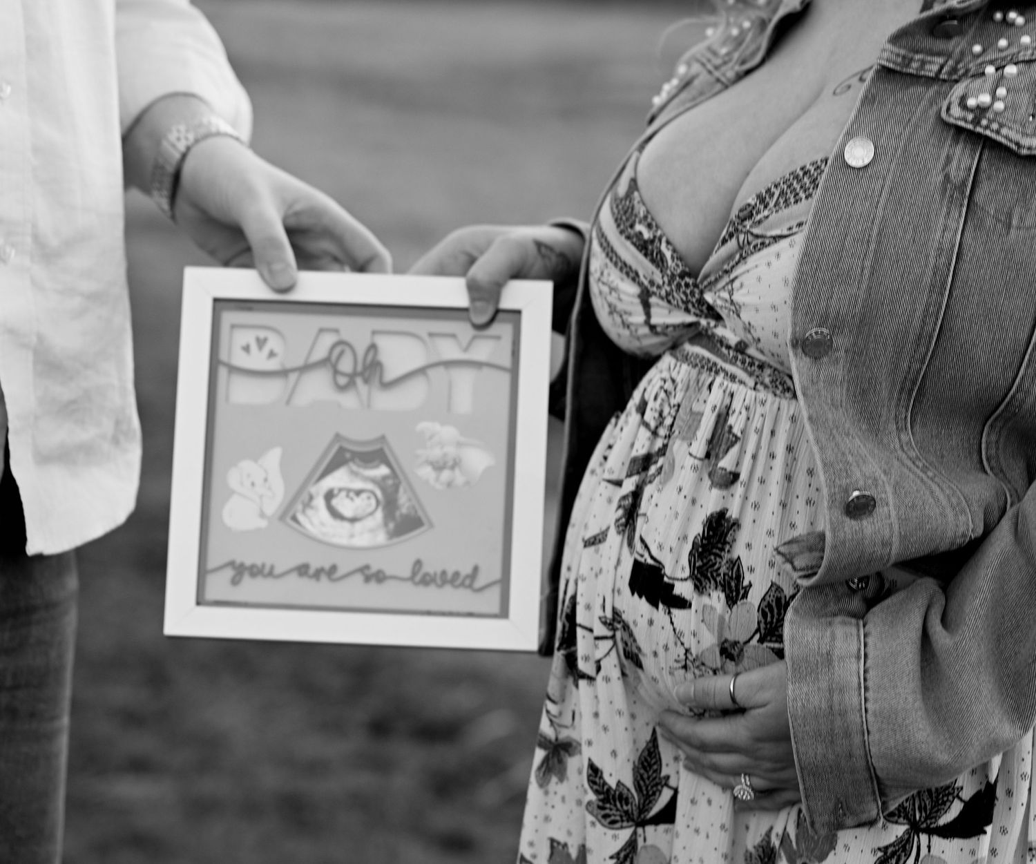 Black and white photo of pregnant woman holding ultrasound artwork with 'you are so loved' text.