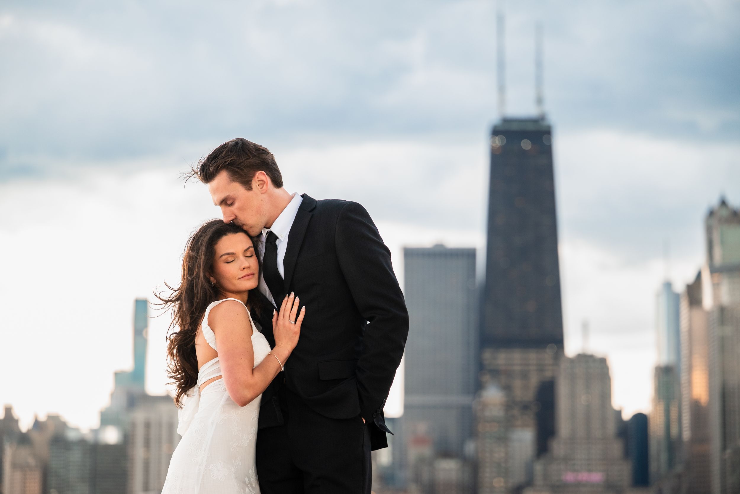 Romantic couple embracing on rooftop with Chicago skyline and John Hancock Center in background on cloudy day.