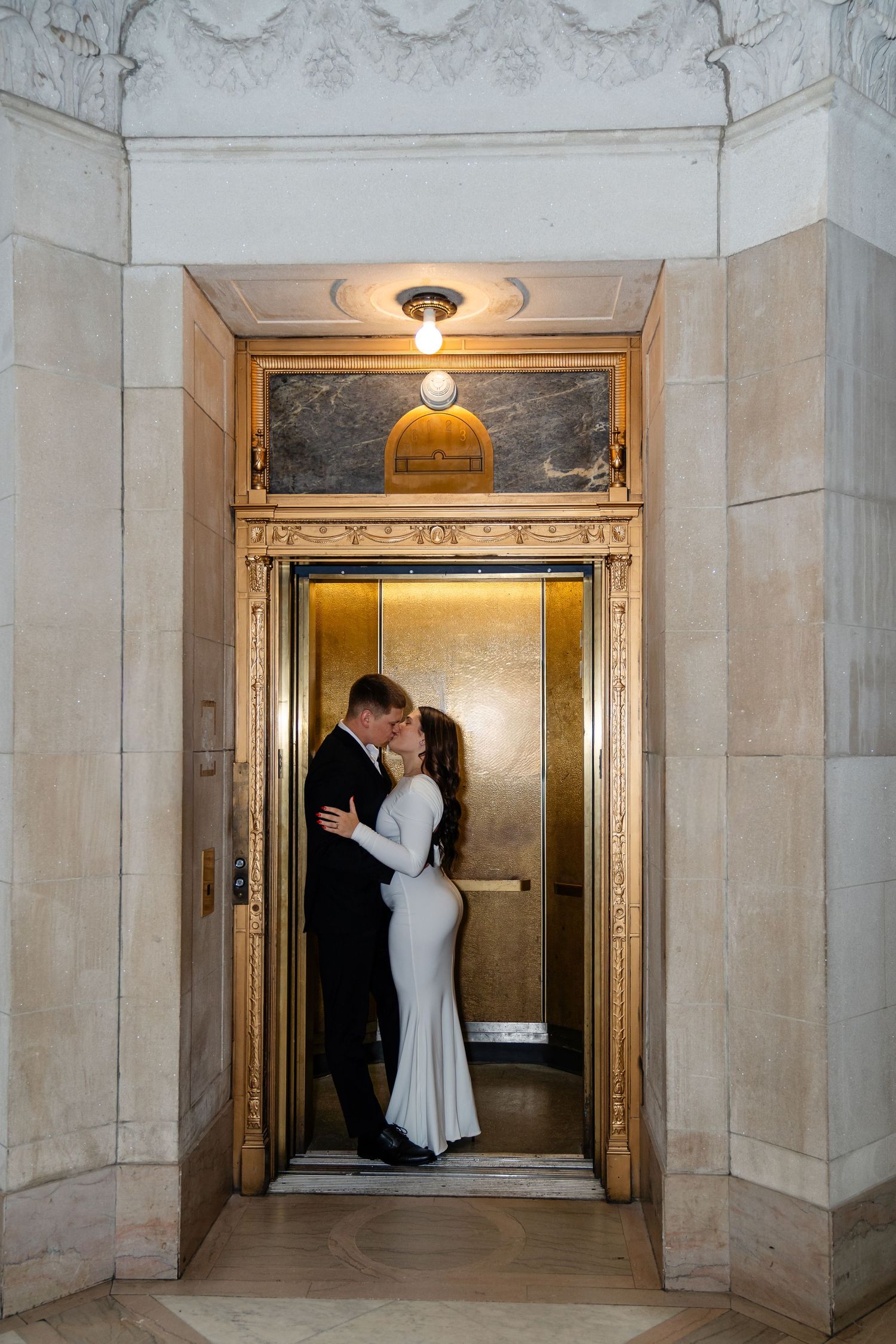 Couple dancing on ornate balcony with golden arch and glowing pendant light in elegant marble building.