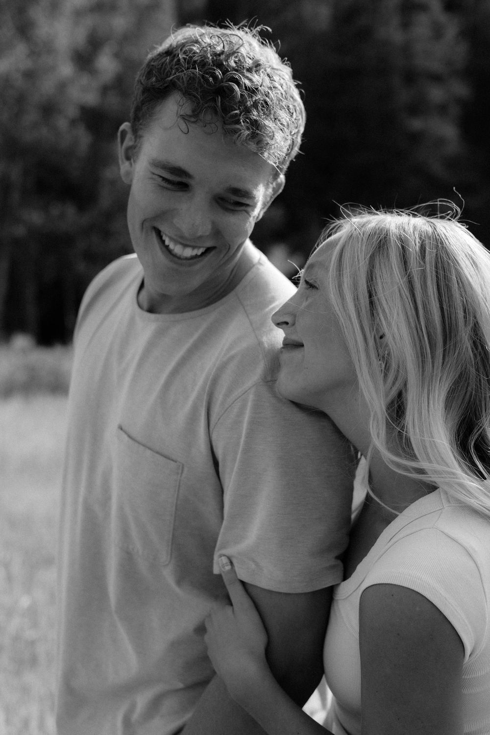 Black and white photo of a laughing couple embracing outdoors, man in t-shirt smiling as woman leans in close.