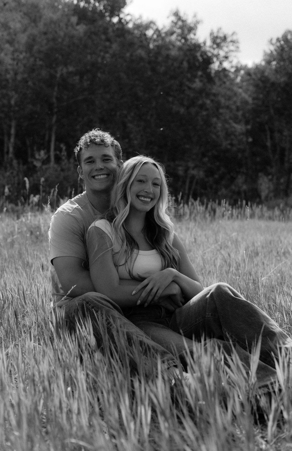 Smiling couple sitting together in a grassy meadow, black and white romantic outdoor portrait.