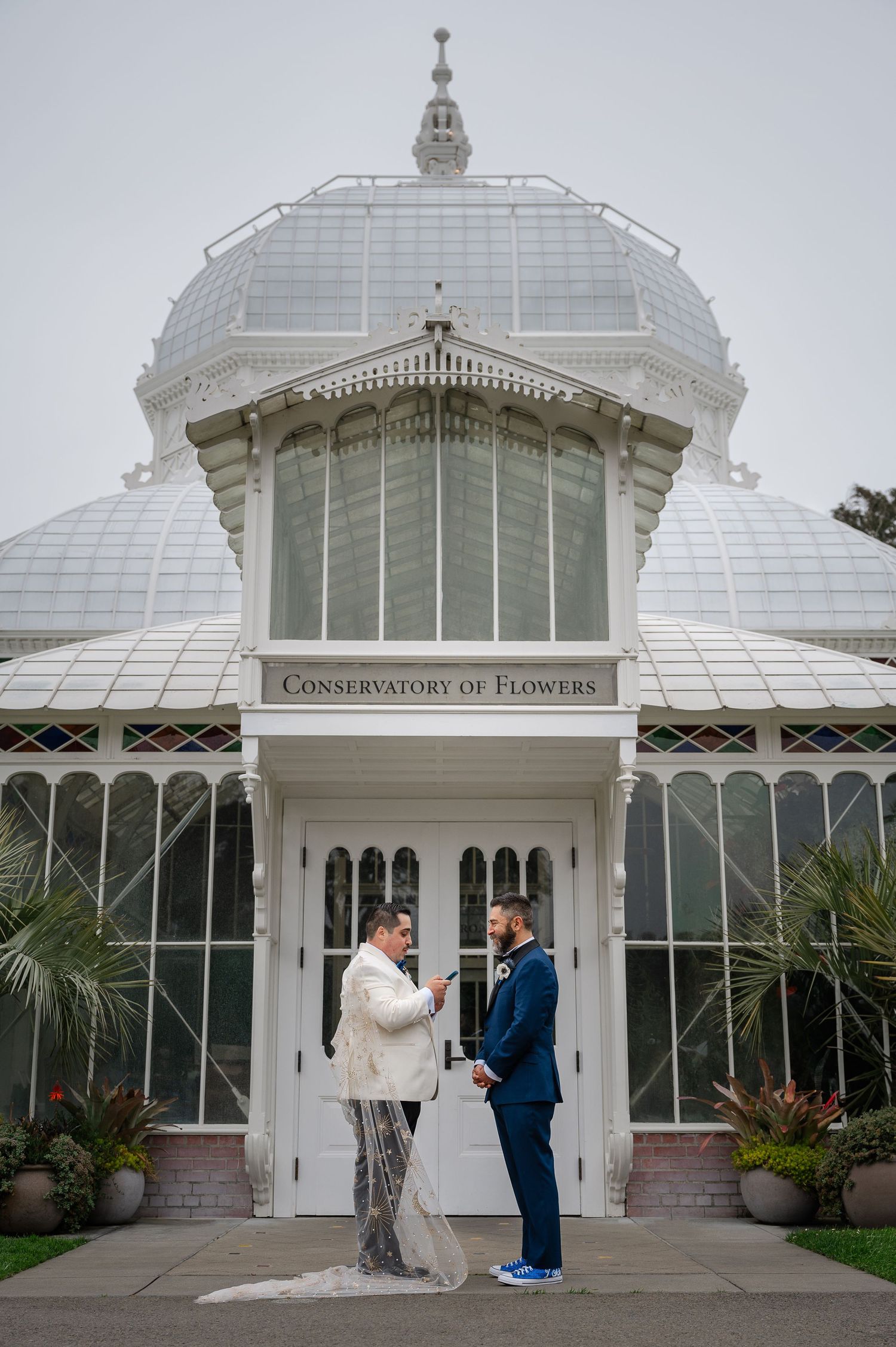Two grooms exchange vows in front of the Conservatory of Flowers in San Francisco on their wedding day.