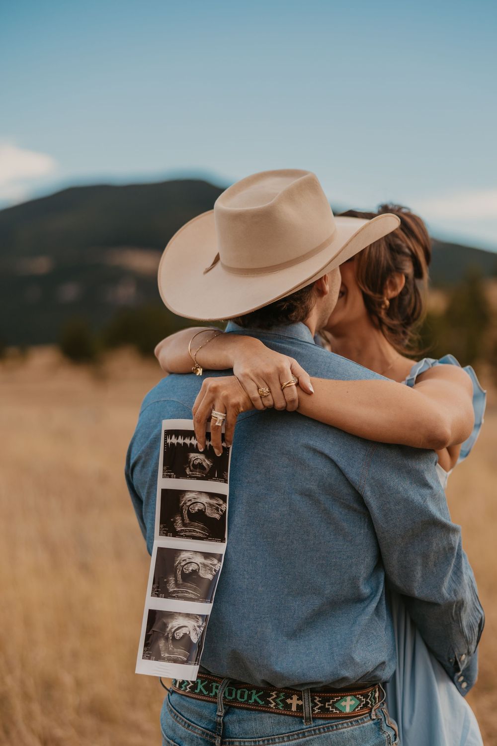 Cowboy holds wife while showing off ultrasound photos in the mountains of Red Lodge, Montana captured by Montana Photographer