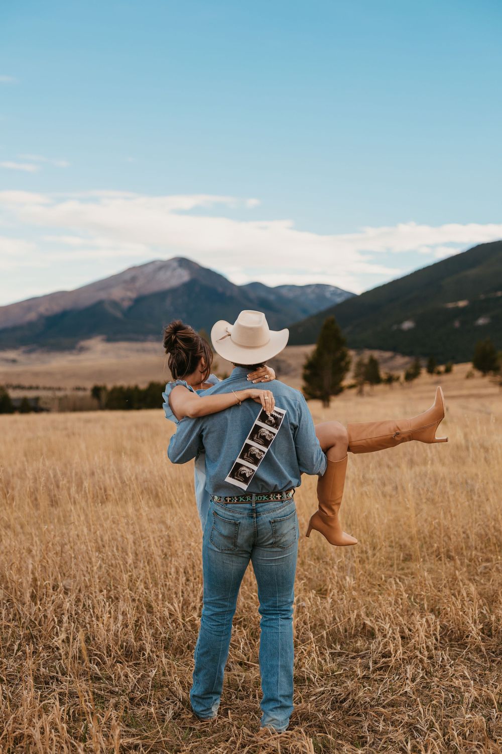 Cowboy carries wife while showing off ultrasound photos in the mountains of Red Lodge, Montana captured by Montana Photographer