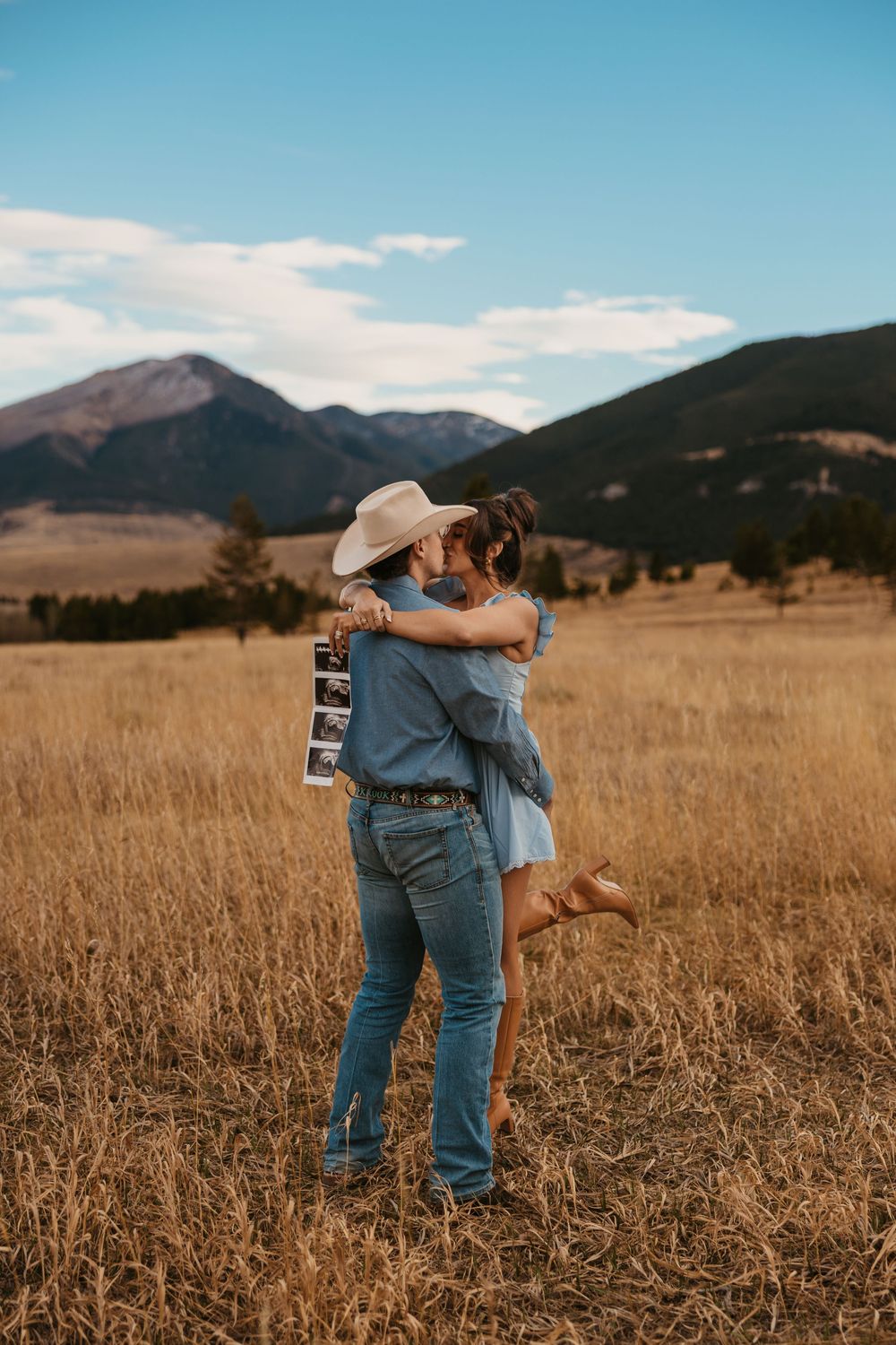 Cowboy holds wife while showing off ultrasound photos in the mountains of Red Lodge, Montana captured by Montana Photographer