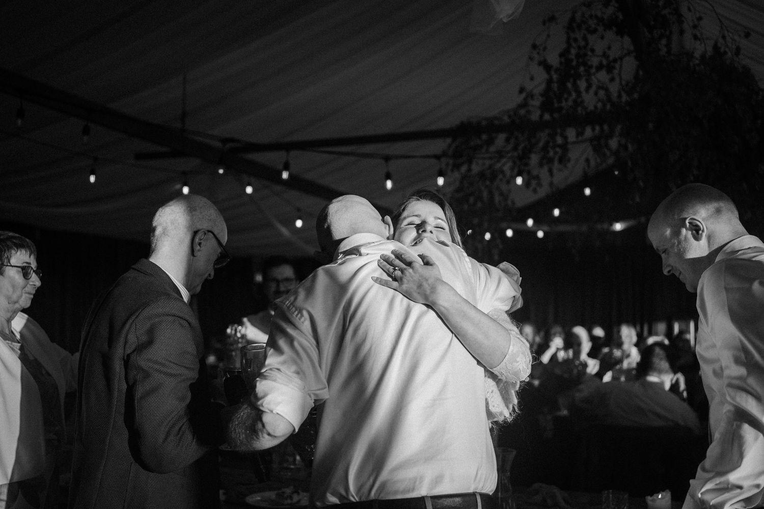 Black and white photo of guests hugging and celebrating on outdoor wedding dance floor.