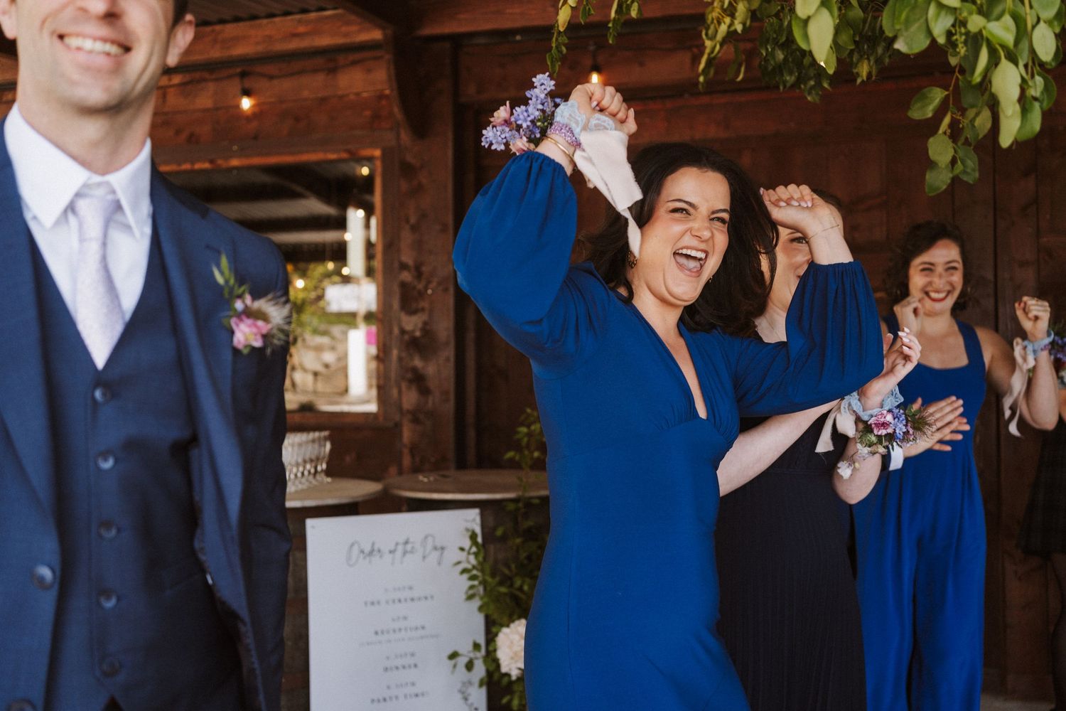 Bridesmaids in royal blue dresses celebrate joyfully at a rustic barn wedding reception.