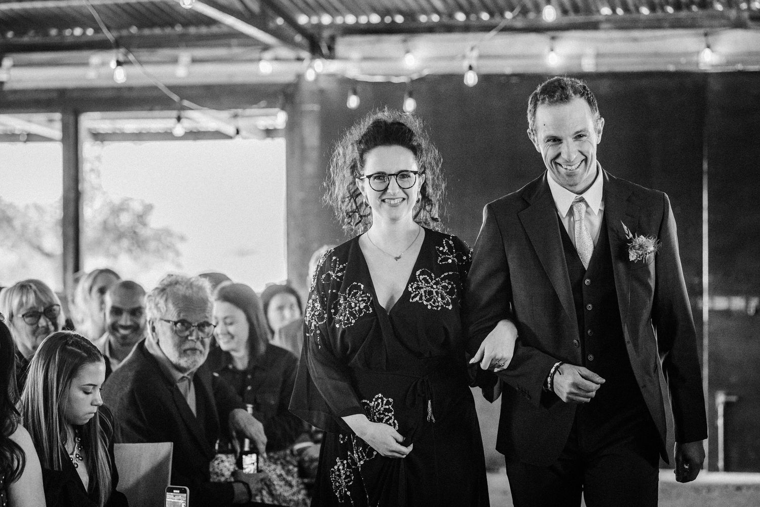 Black and white photo of a smiling bride and groom walking arm in arm at their wedding reception.