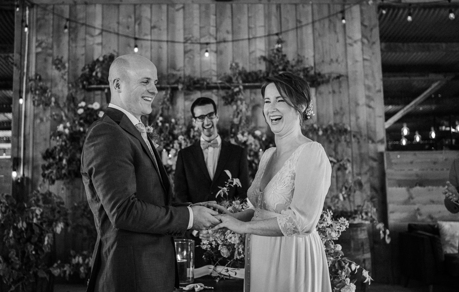 Black and white photo of a couple exchanging vows at a rustic barn wedding ceremony with an officiant.