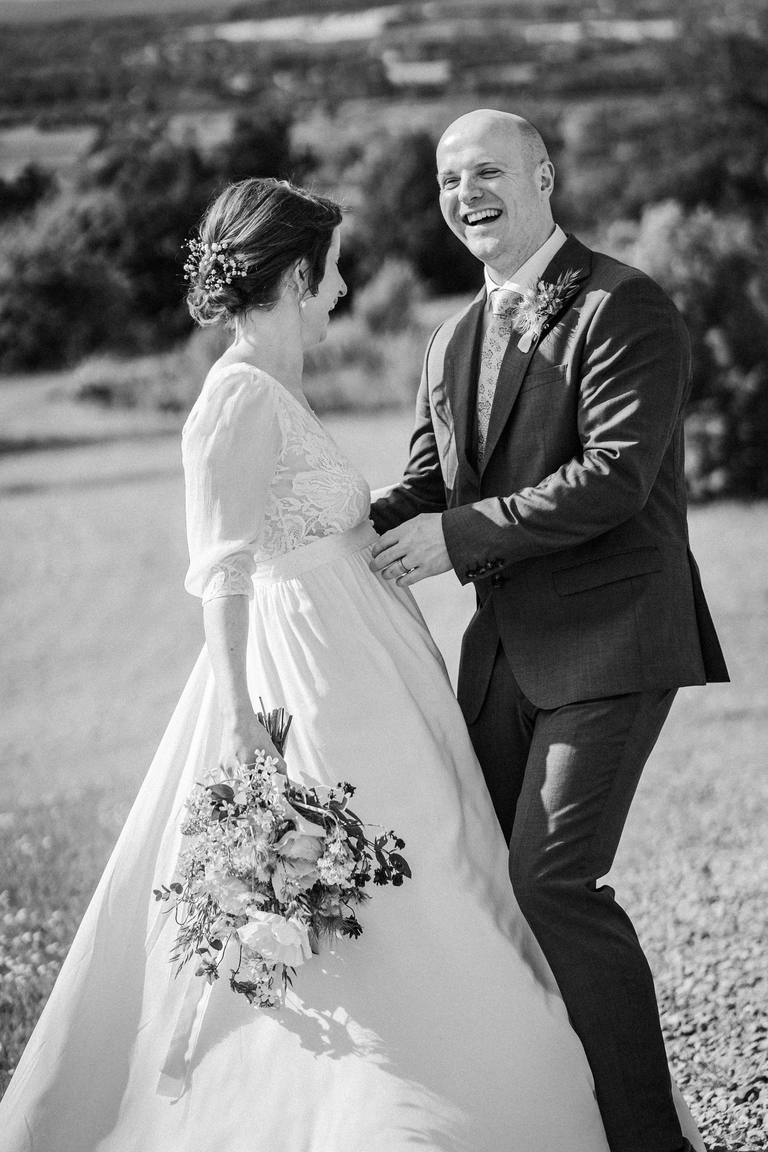 Black and white photo of smiling bride and groom walking together outdoors holding a bouquet on their wedding day.