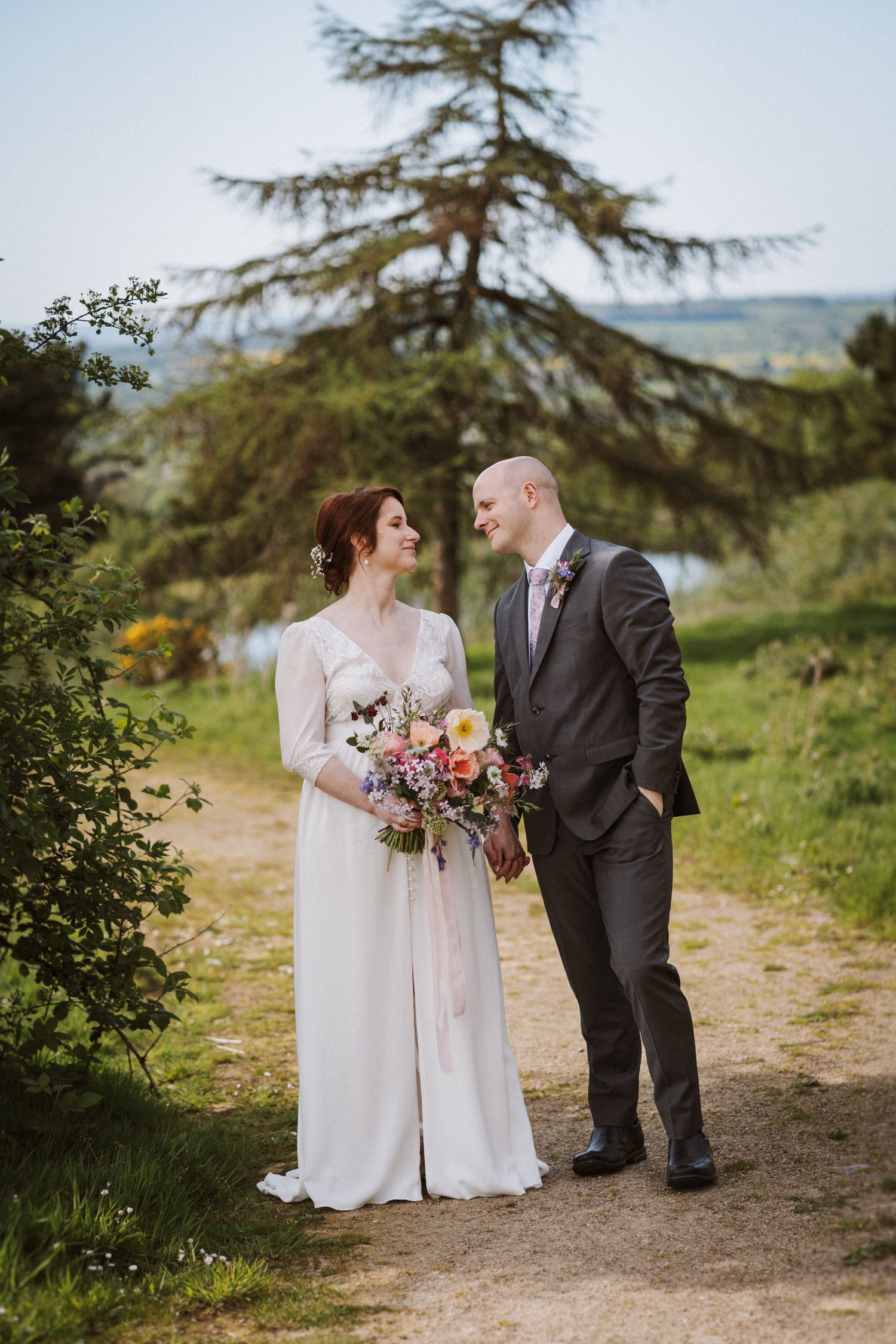 A bride and groom share a romantic moment on a garden path, with the bride holding a colorful bouquet.