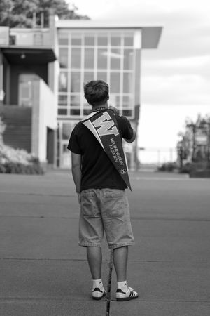 Black and white photo of a student holding a University of Washington pennant flag outside a modern building.