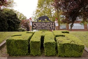 Two students stand atop sculpted hedges spelling SHS at Snohomish High School entrance sign.