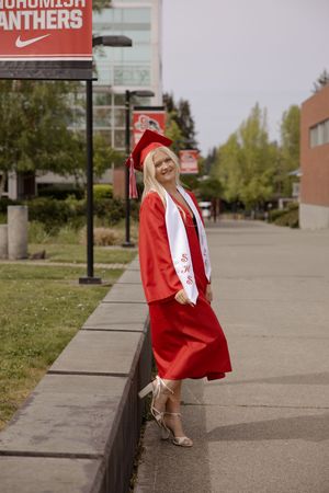 Female graduate in red cap and gown poses confidently outside Snohomish Panthers high school campus.