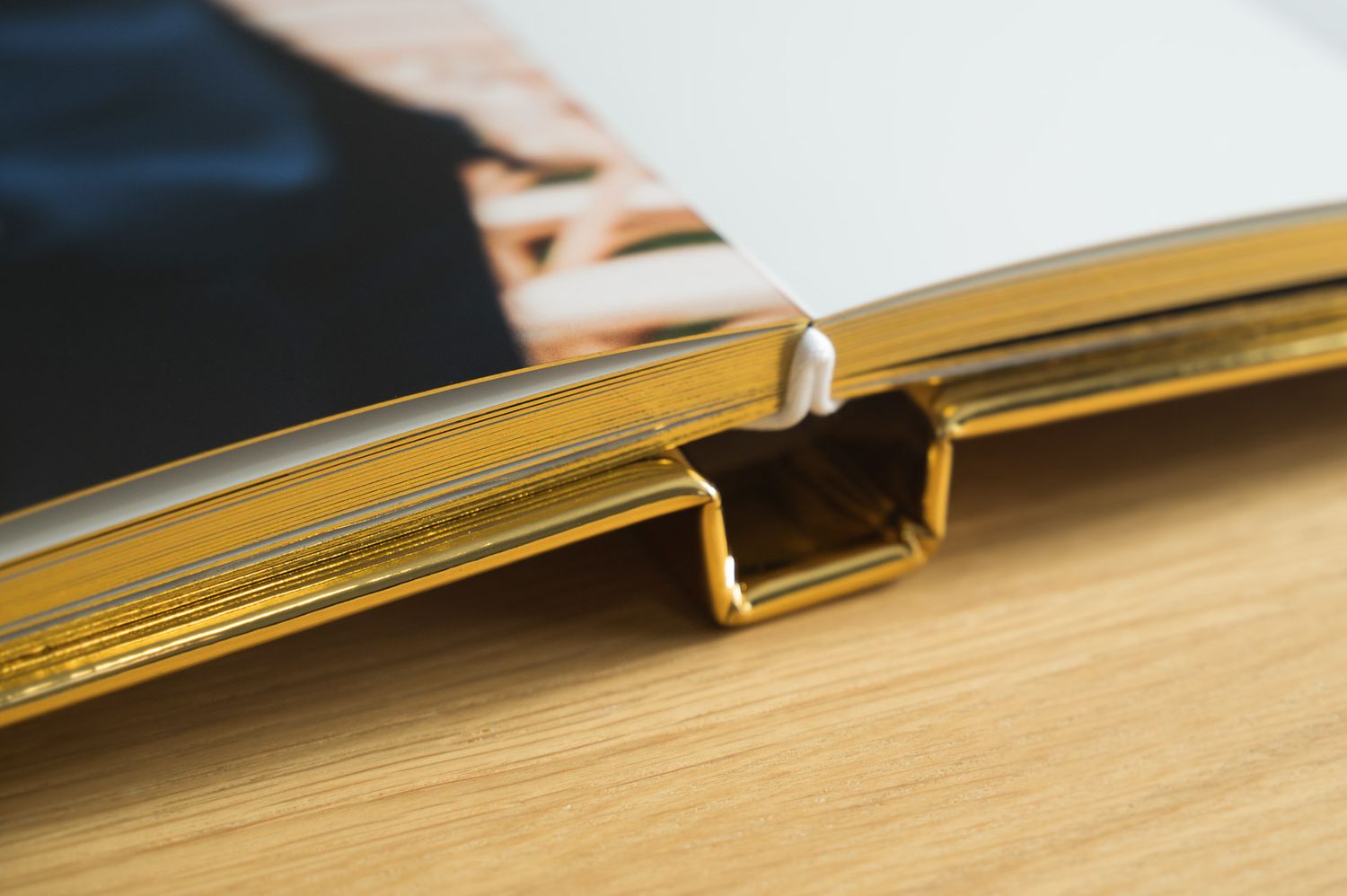 Close-up of a gold metallic photo book spine with a binder clip on a wooden surface.