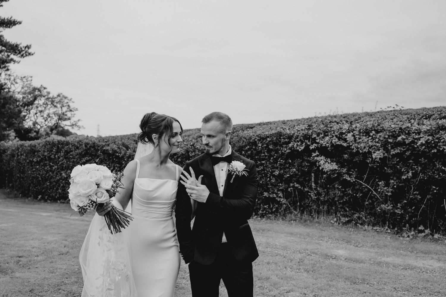Black and white photo of a bride and groom sharing a tender moment outdoors, bride holding a white bouquet.