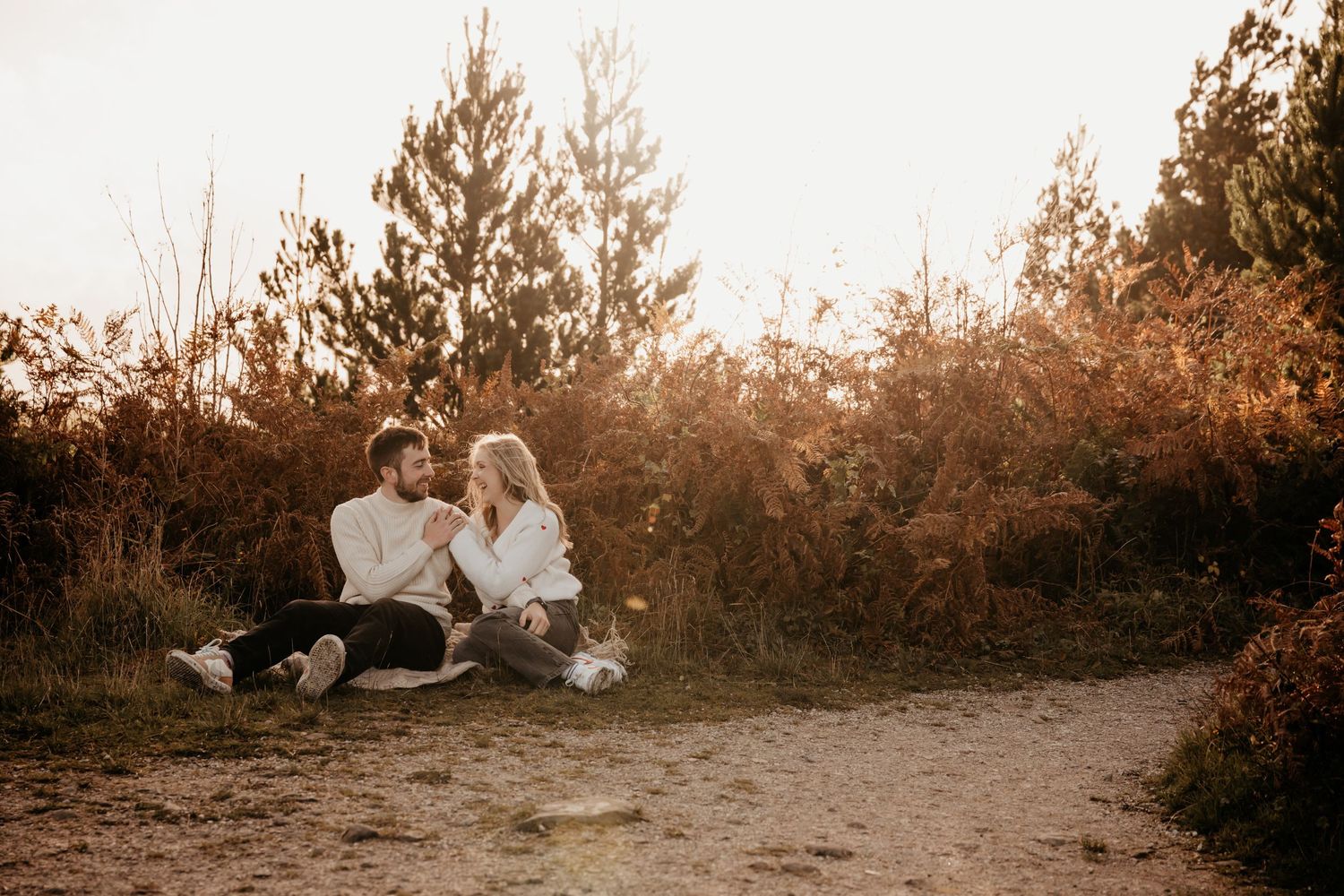 Couple sitting together on sandy path surrounded by autumn foliage in warm golden sunset light.