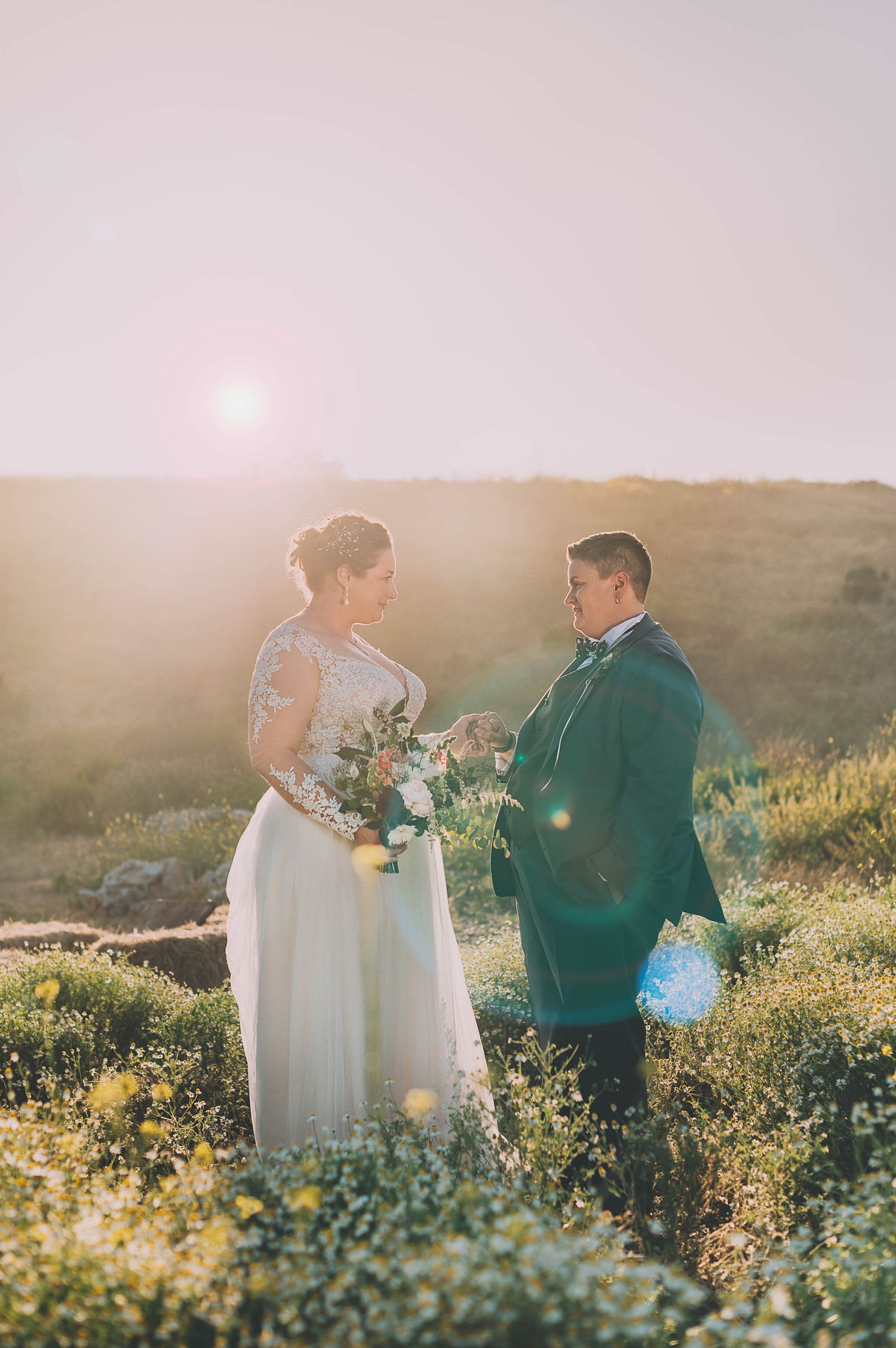A dressed up couple crosses a small stream in a lush forest setting during what appears to be a wedding photoshoot.