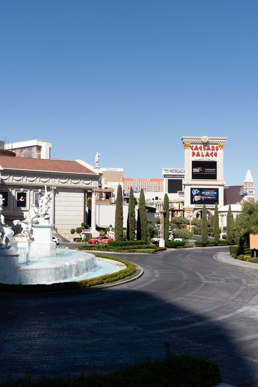 Caesars Palace casino entrance with ornate fountain and lush landscaping on the Las Vegas Strip under clear blue sky.