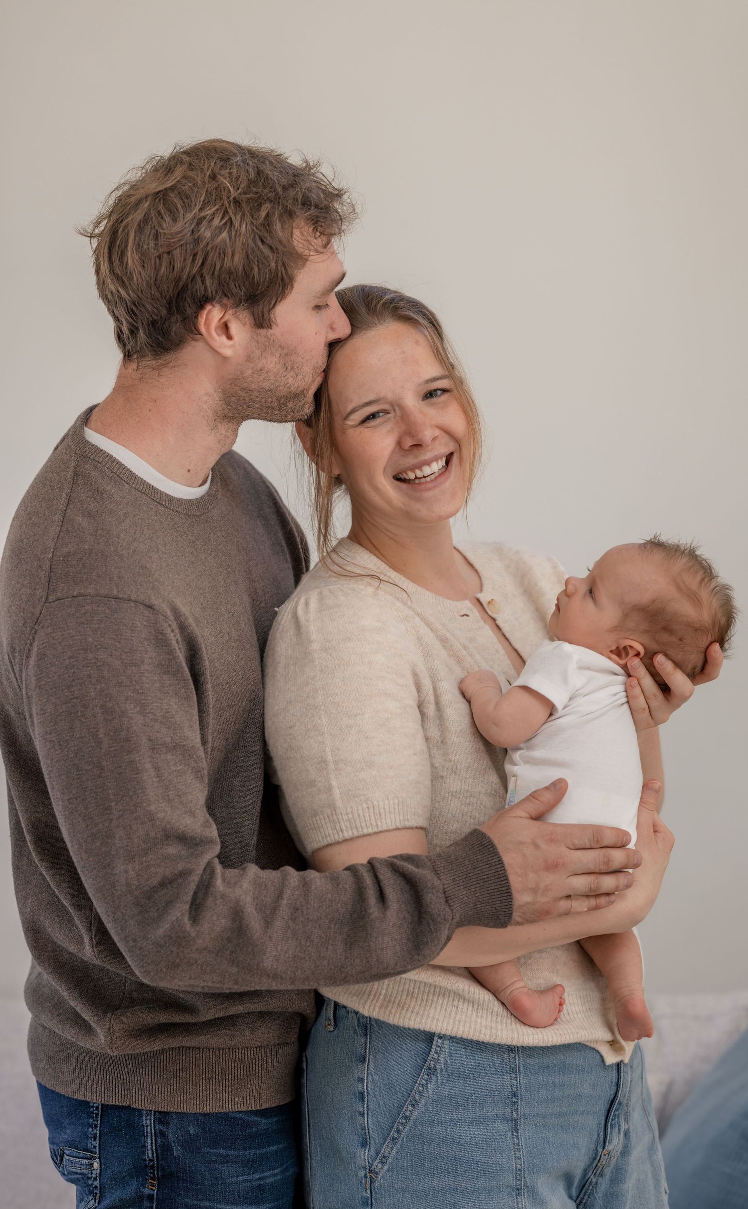 Happy young couple smiling and cuddling while lovingly holding their newborn baby together indoors.