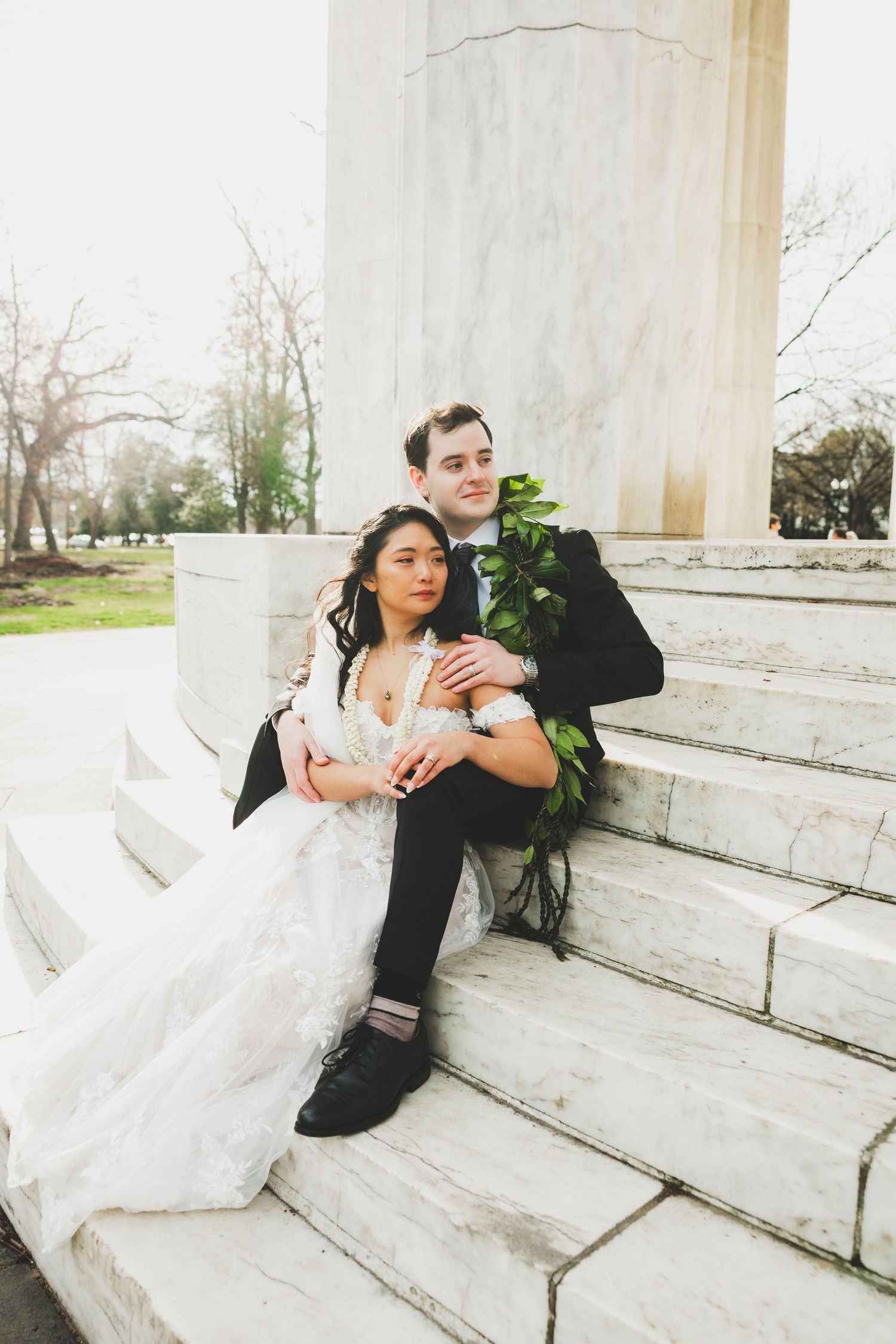 Bride and groom sitting on marble steps at Dc WWII Memorial, sharing a romantic embrace after the intimate wedding