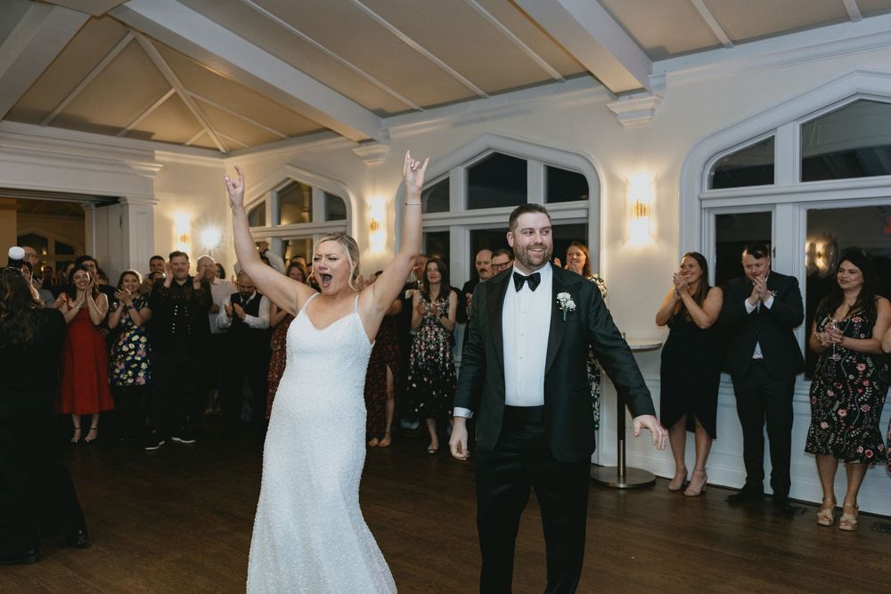 Bride and groom make grand entrance at elegant wedding reception as guests cheer and applaud in decorated ballroom.