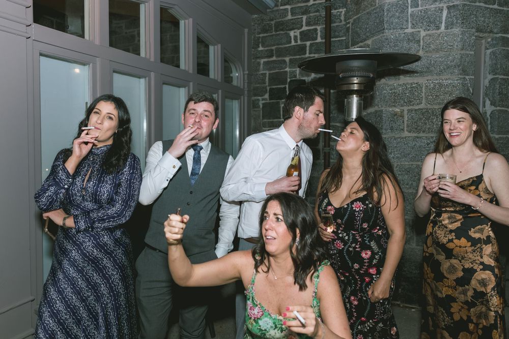 Group of young adults laughing and socializing at a wedding reception party indoors.