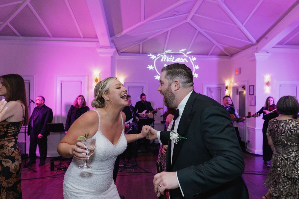 Bride and groom laughing and dancing together at their wedding reception with a live band performing in the background.