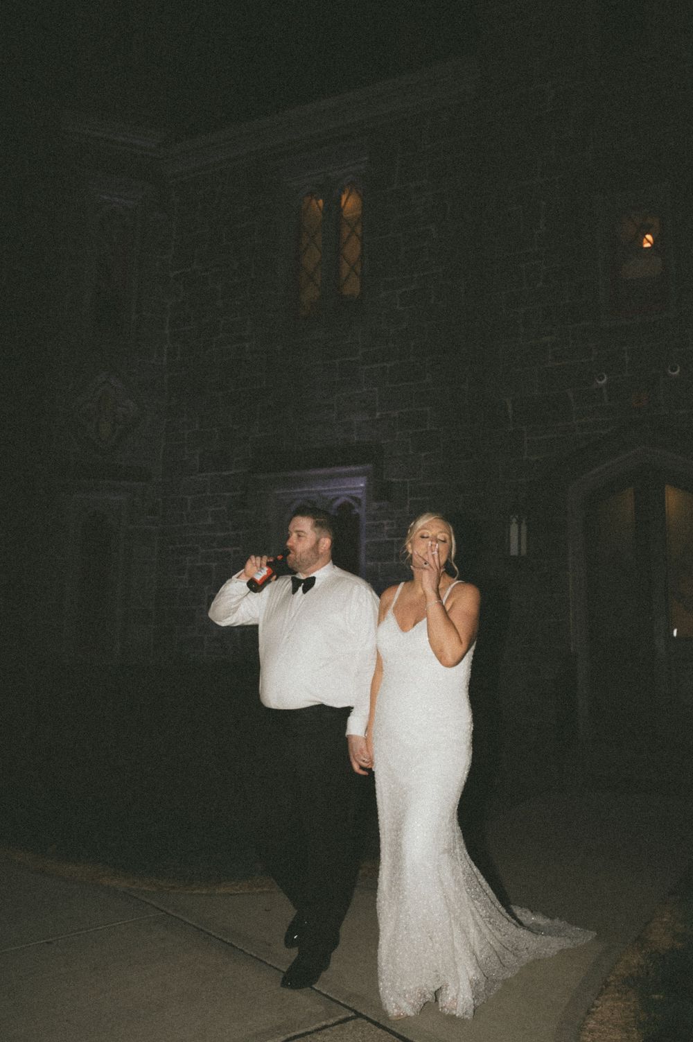 Bride and groom sharing a joyful moment outside a stone castle venue at night in wedding attire.
