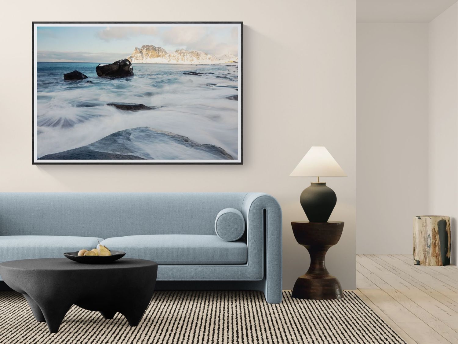 Framed coastal seascape print with crashing waves and rocky cliffs displayed above a blue sofa.