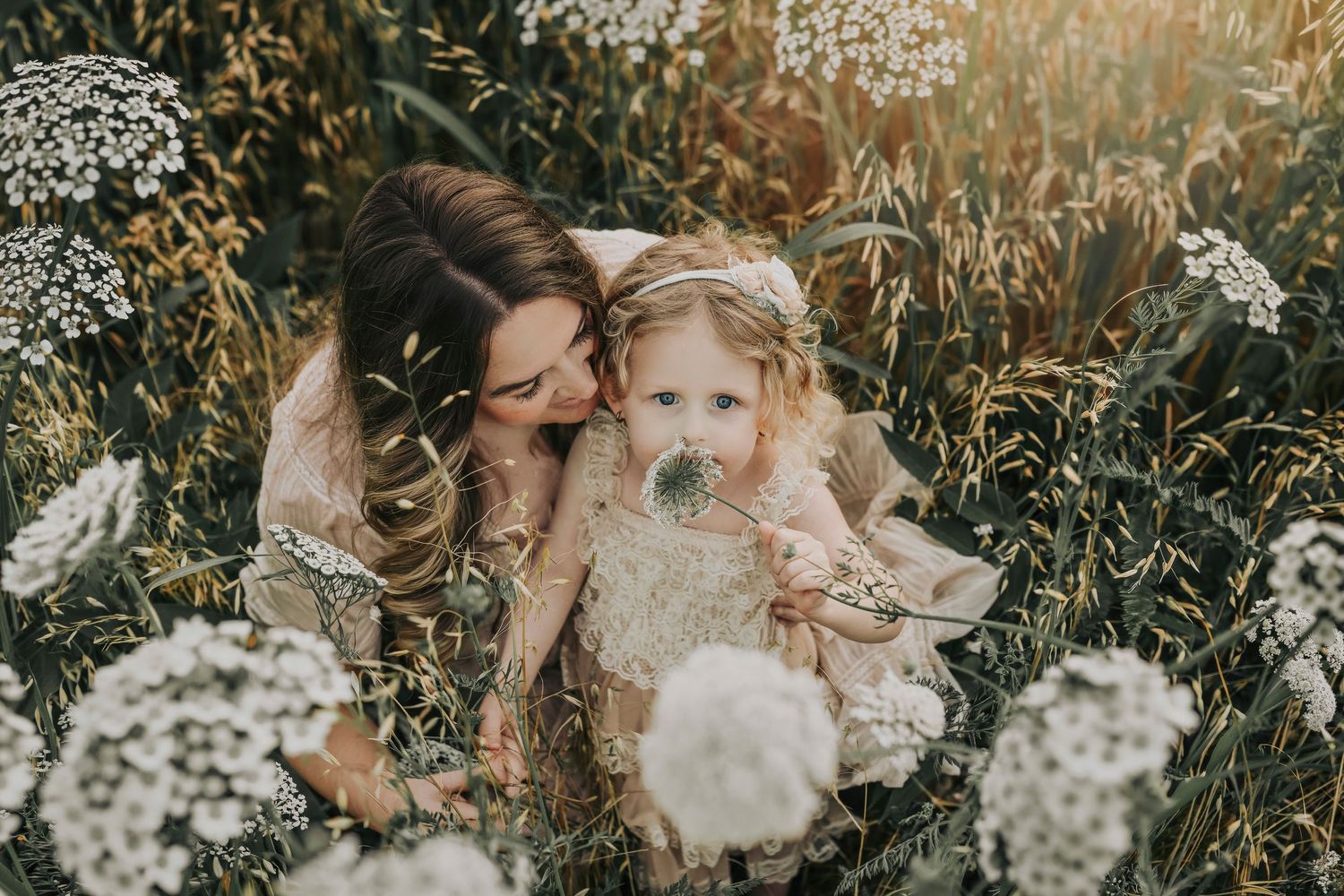 a little girls smells a flower as her mother cradles her in a field of white wildflowers at white rock lake