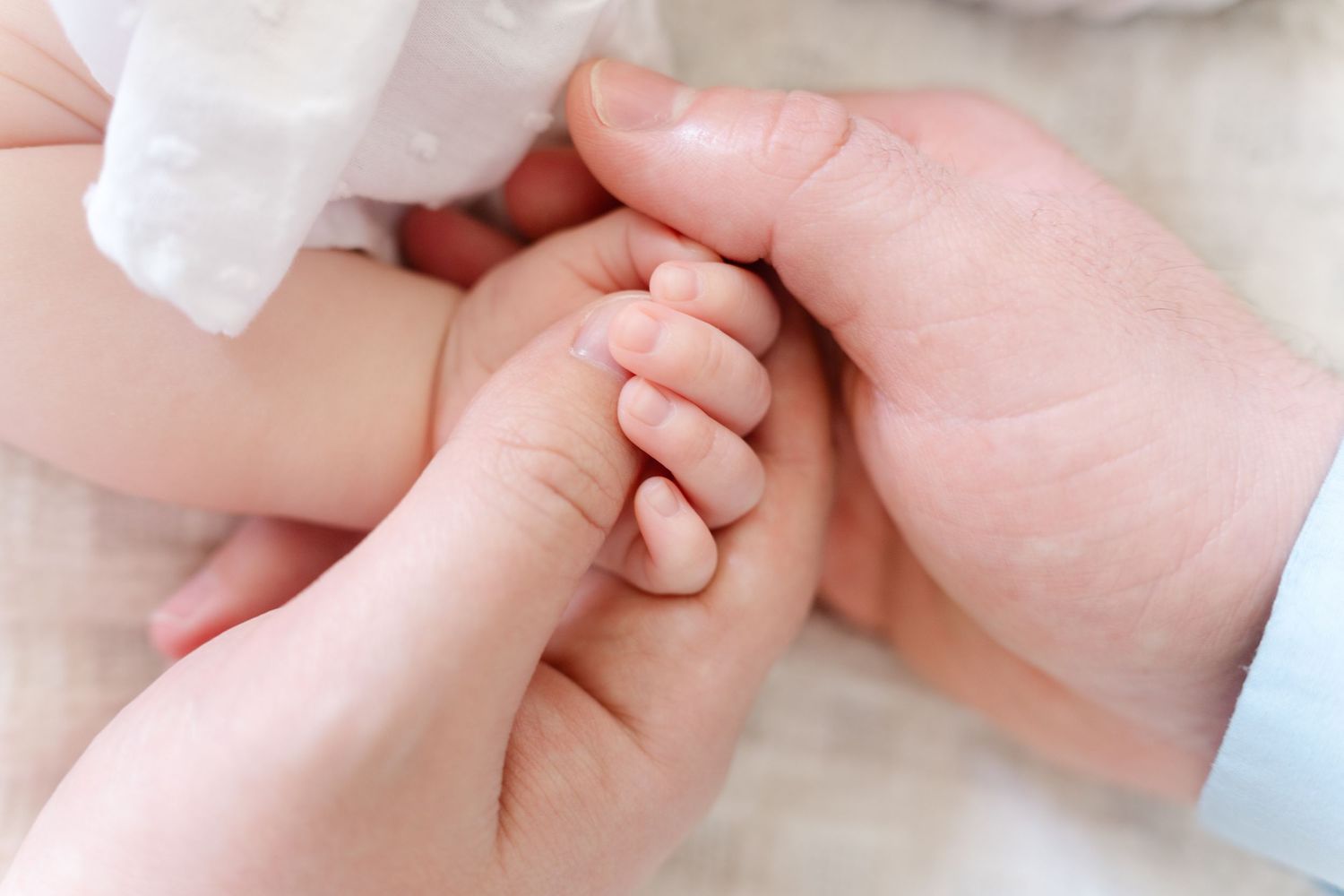 Parents' hands gently holding a tiny newborn baby's hand in newborn photoshoot session.