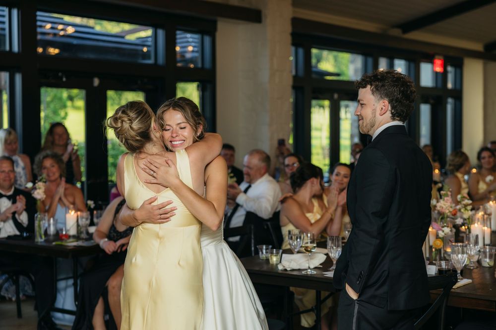Bride in white gown hugging her maid of honor in yellow dress at wedding reception captured by candid photographer in Wisconsin