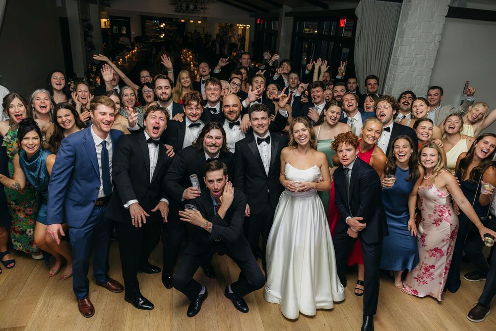 A joyful wedding reception group photo with bride in white gown and groom in tuxedo captured by candid photographer in Wisconsin