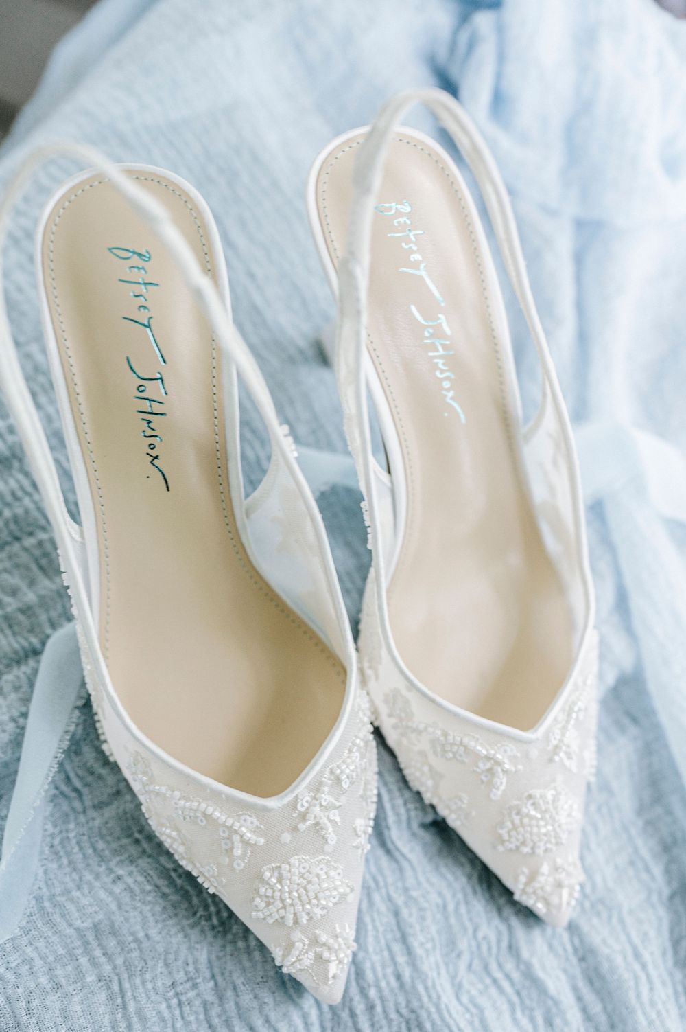Elegant Betsey Johnson white beaded slingback heels on blue fabric, perfect bridal wedding shoes.
